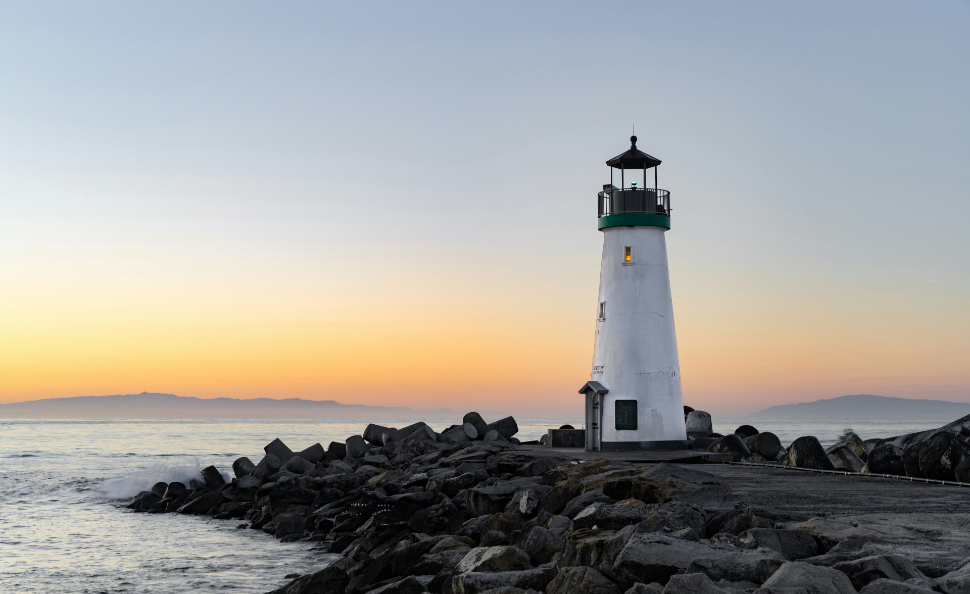 Lighthouse at sunrise on a rocky jetty by the ocean